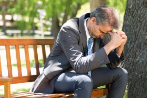 Upset mature businessman sitting on park bench